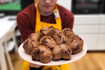 Dziecko trzyma talerz wypełniony czekoladowymi muffinami. W tle przestrzeń kuchni.