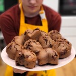 Dziecko trzyma talerz wypełniony czekoladowymi muffinami. W tle przestrzeń kuchni.